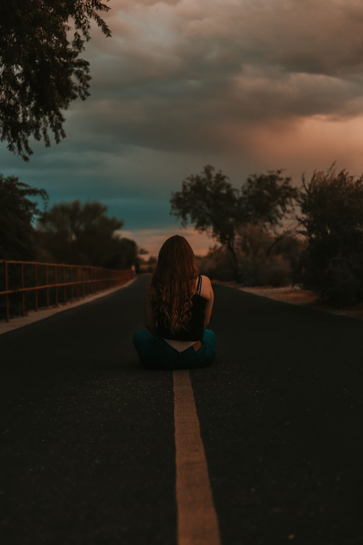 a woman sitting on the side of a road with her back turned to the camera