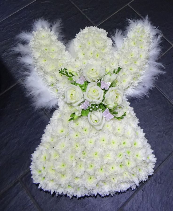 a teddy bear made out of white flowers and feathers on a tile floor with black tiles