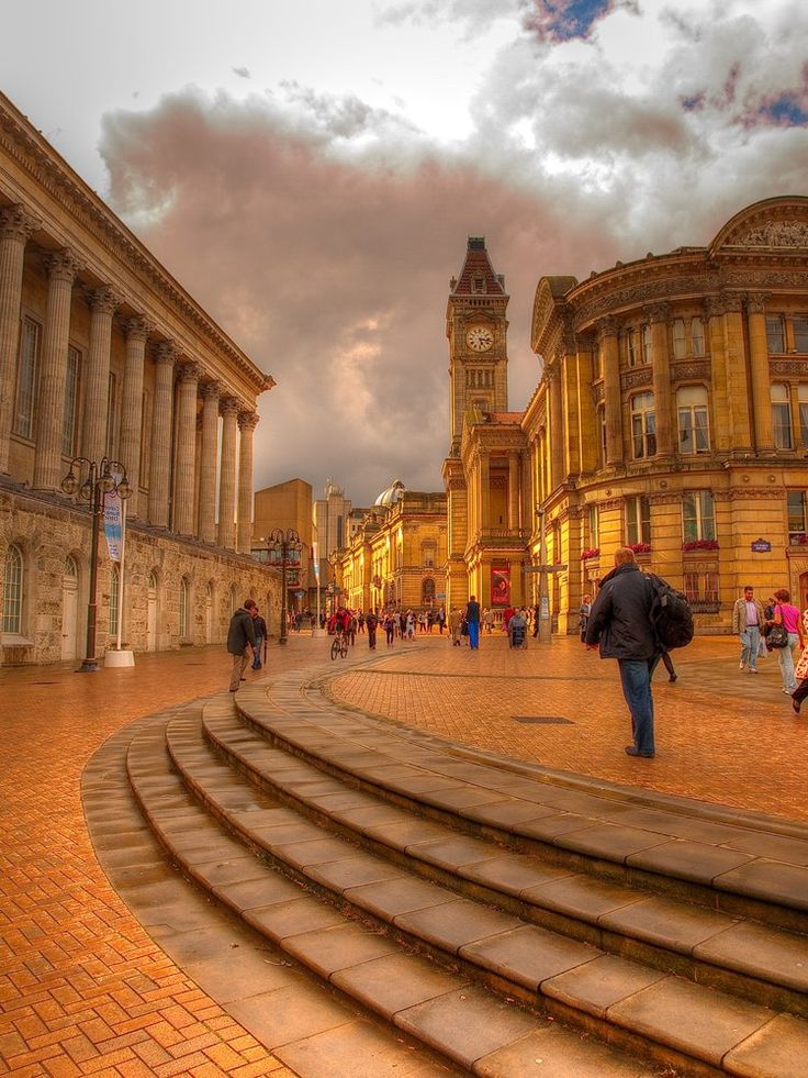 people are walking down the steps in front of some old buildings and clocktowers