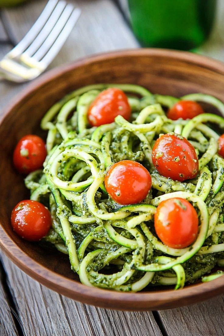 a wooden bowl filled with pesto pasta and cherry tomatoes on top of green sauce