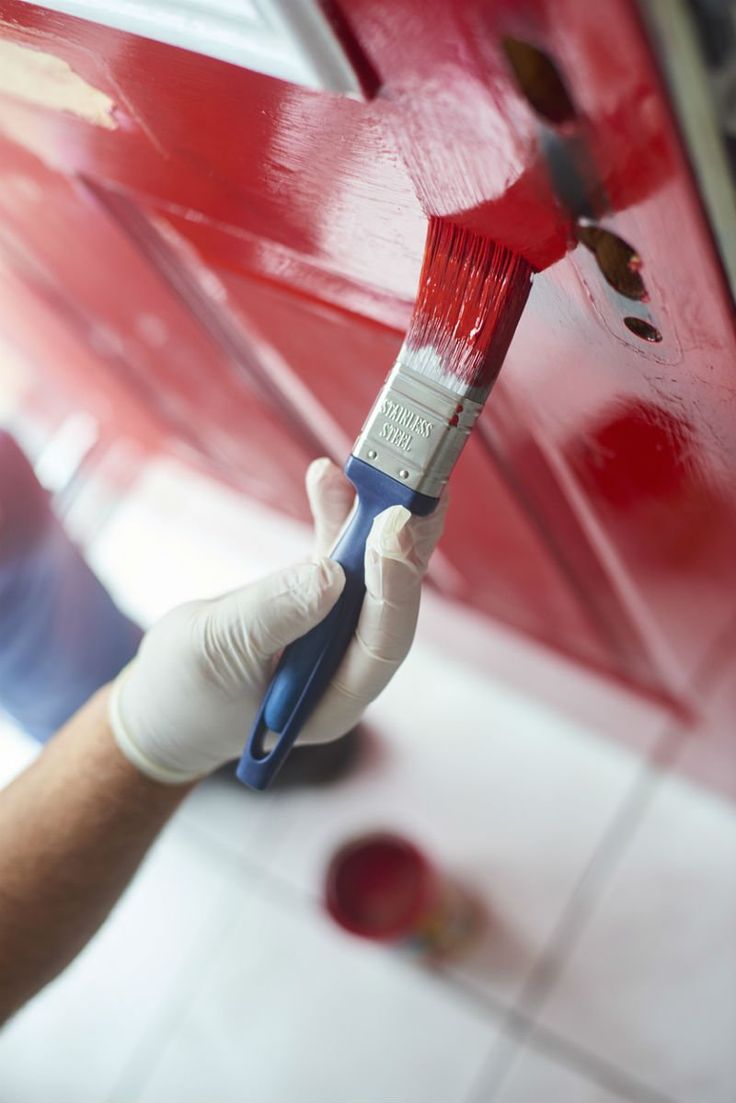 a person holding a paintbrush in their hand while painting a red door with white paint