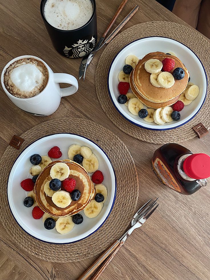 two plates topped with pancakes and fruit next to a cup of coffee