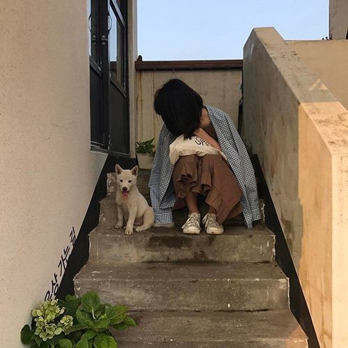 a woman is sitting on the steps with her dog and looking at something in front of her