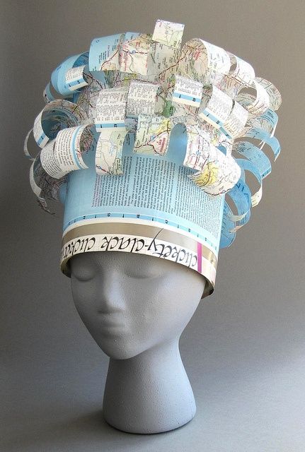 a white mannequin head wearing a hat made out of books and newspaper strips