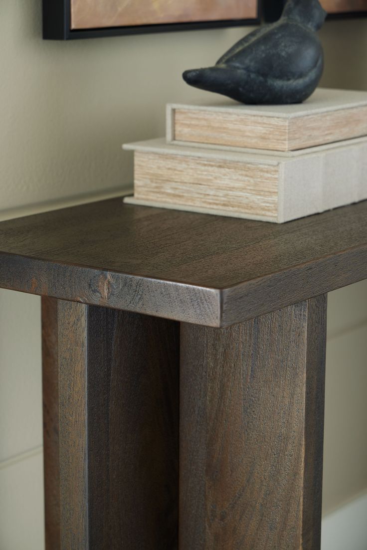 a wooden table topped with two books and a bird figurine on top of it