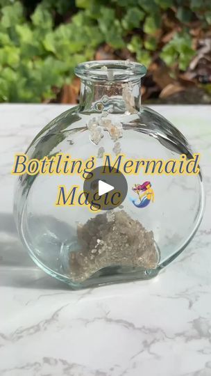 a glass bottle filled with sand sitting on top of a white marble counter next to plants