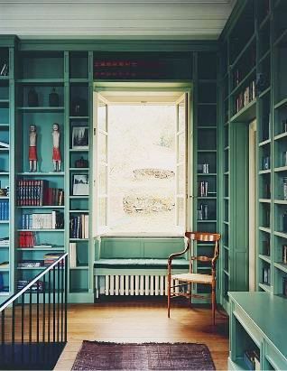 a room with green bookshelves and a chair in the corner next to a window