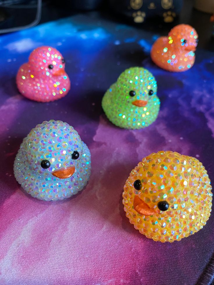 five colorful rubber ducks sitting on top of a purple cloth covered table with sequins