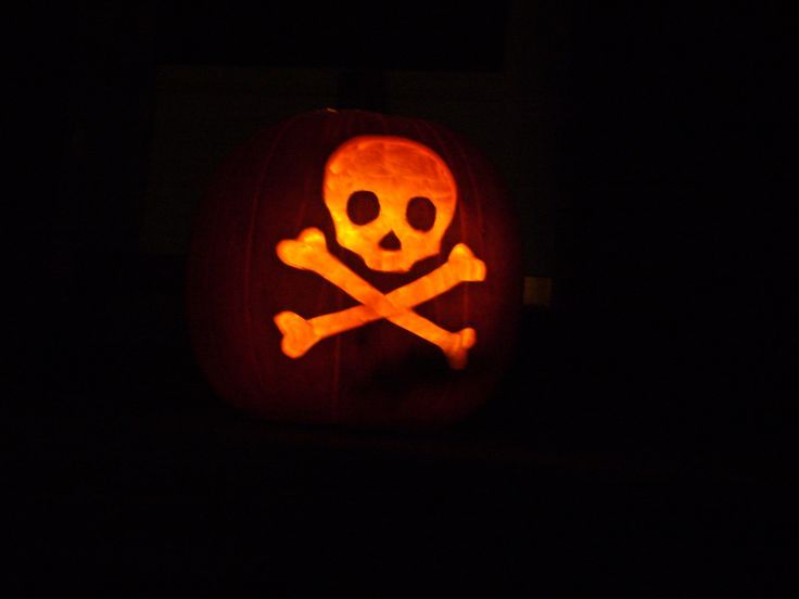 a pumpkin carved to look like a skull and crossbones is lit up in the dark