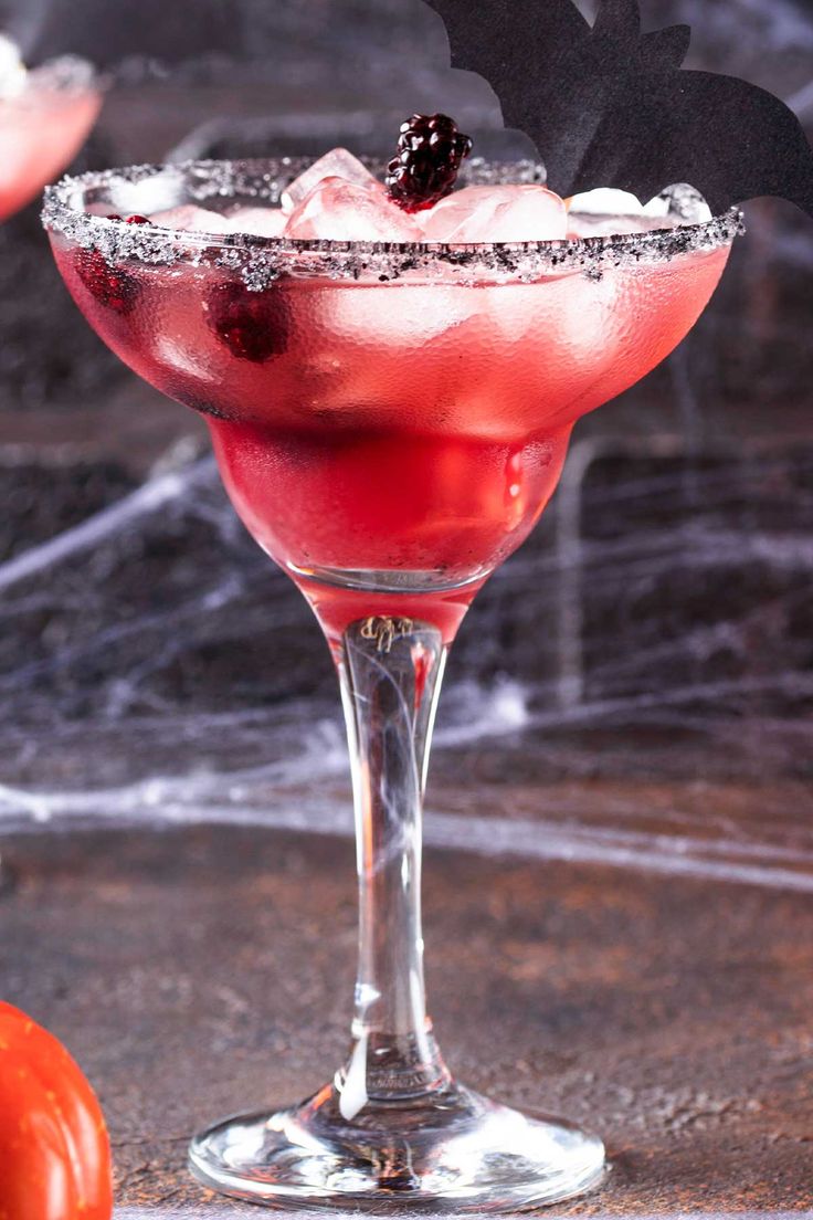 a halloween drink in a wine glass with a bat decoration on the rim