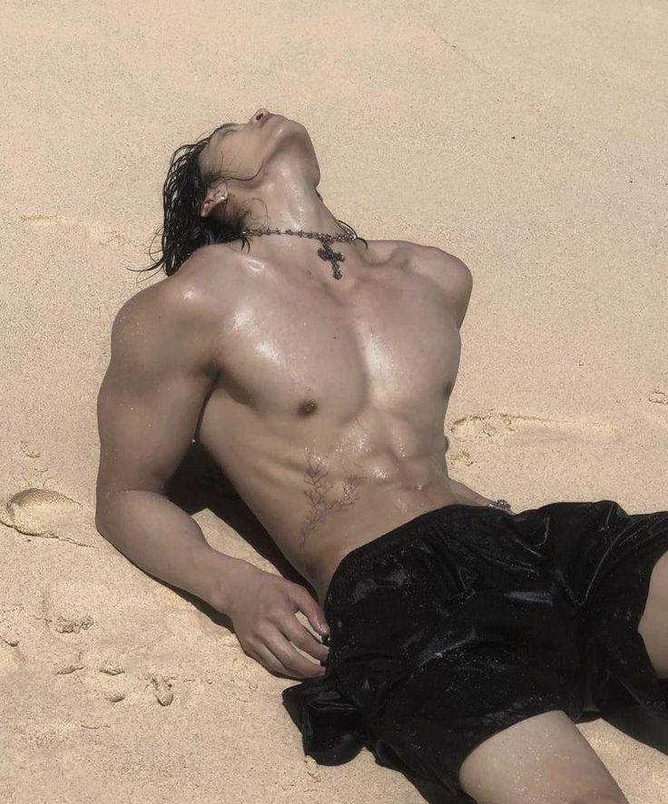 a shirtless man laying on the sand with his head in his hands and eyes closed