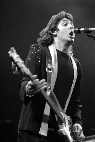 a man holding a guitar and singing into a microphone while standing in front of a microphone