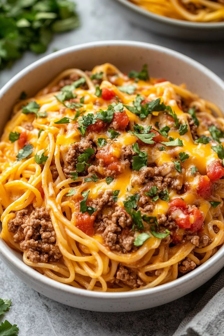 a white bowl filled with spaghetti topped with ground beef and cheese, garnished with parsley