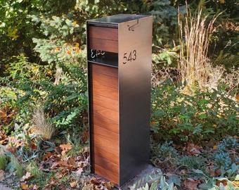 a mailbox sitting on the side of a road in front of some bushes and trees