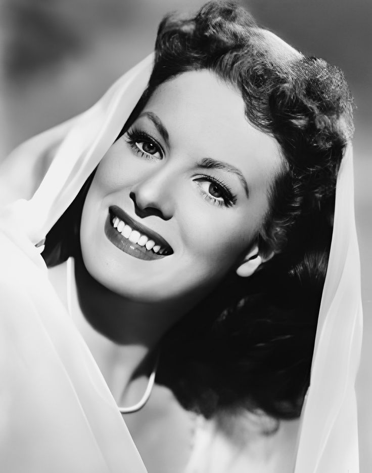 a black and white photo of a woman with a veil on her head, smiling