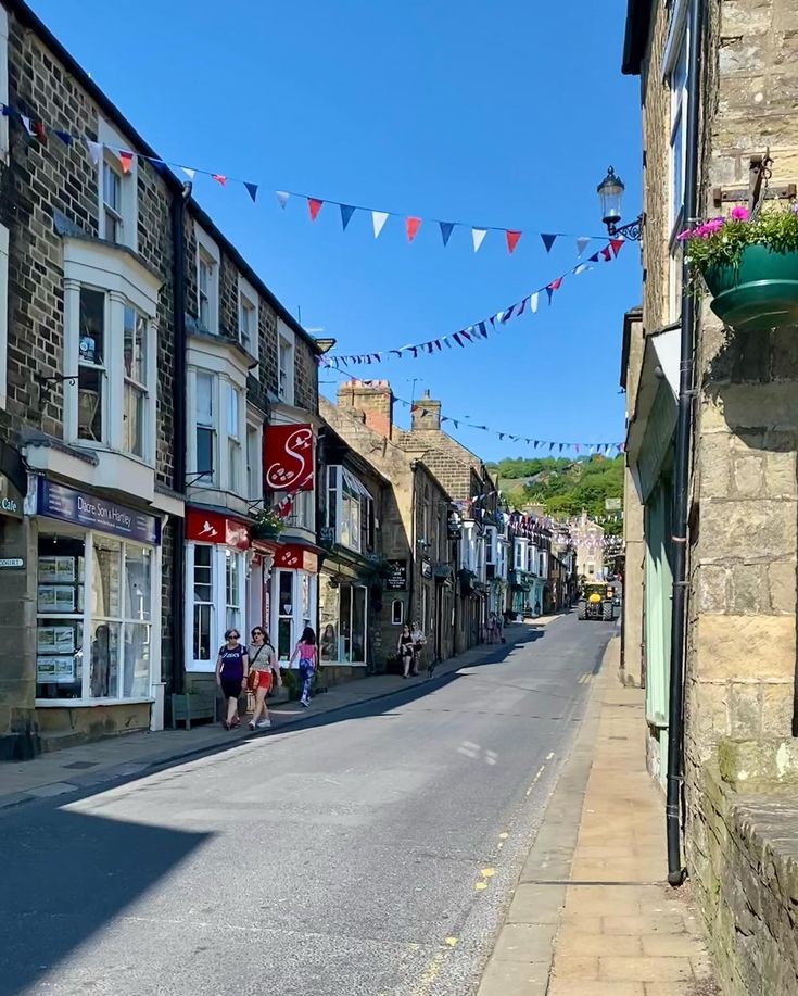 people are walking down the street in an old town with flags strung from buildings on both sides