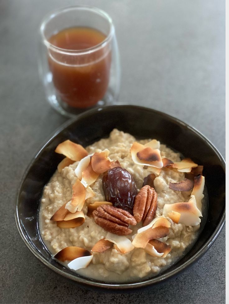 a bowl of oatmeal topped with nuts next to a cup of tea