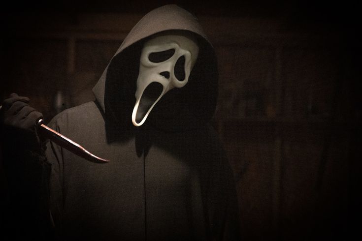 a person wearing a mask and holding a knife in the dark with a ghost face on it