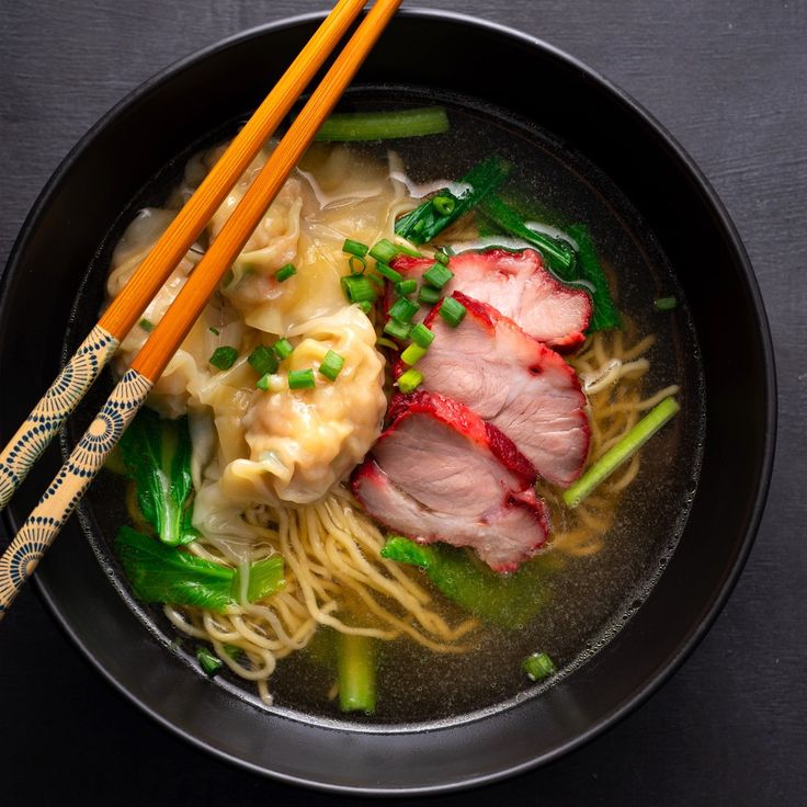 two chopsticks sit on top of a bowl of noodles with meat and veggies