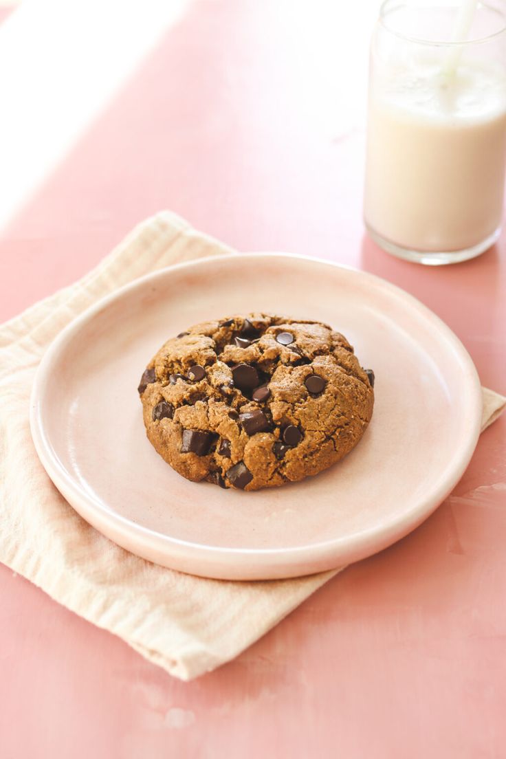 a chocolate chip cookie on a plate next to a glass of milk