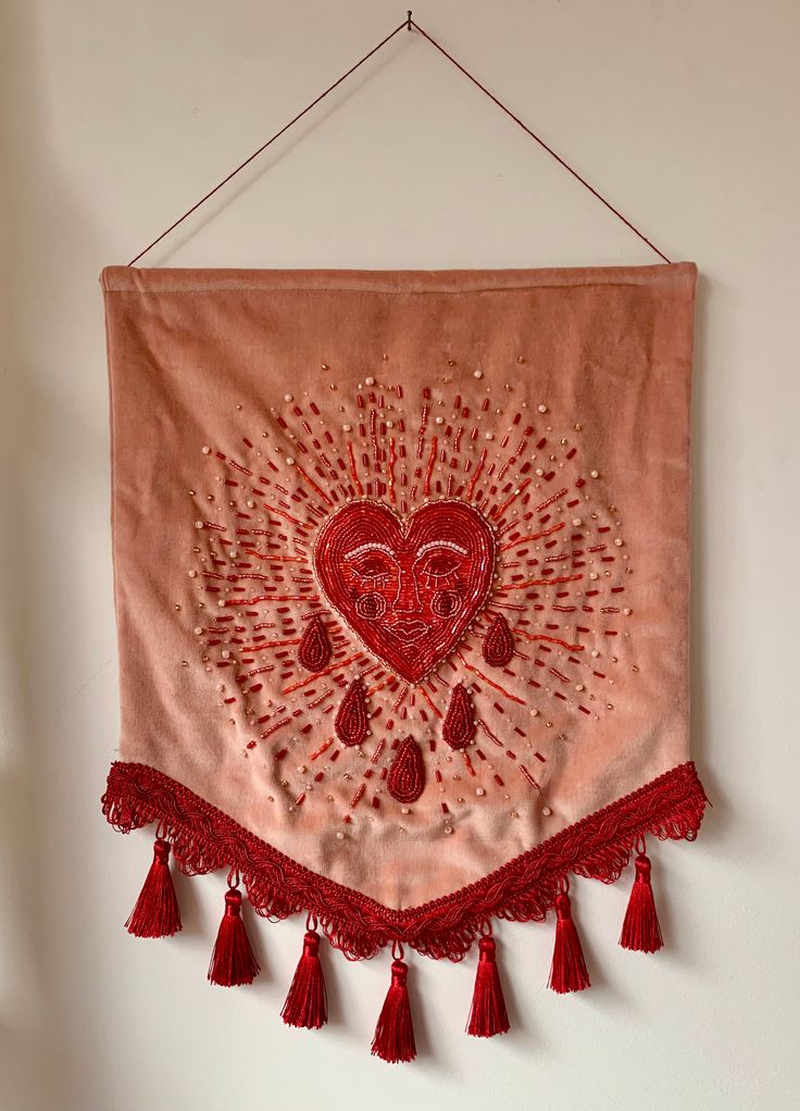 a wall hanging with red tassels and a heart on the front, attached to a white wall