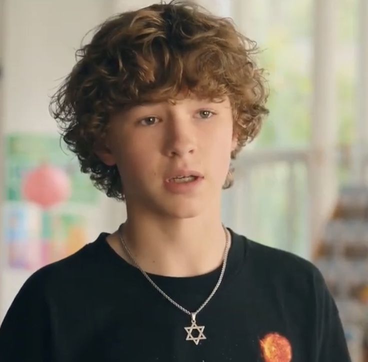 a young boy with curly hair wearing a star of david necklace and looking at the camera