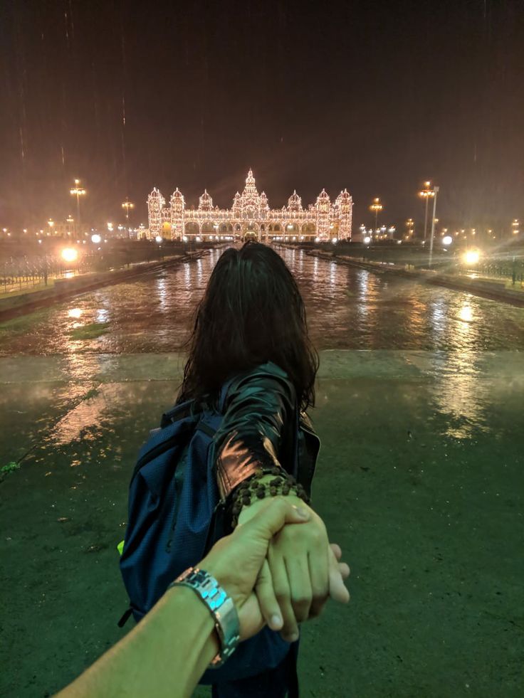 a person holding the hand of another person in front of a body of water at night