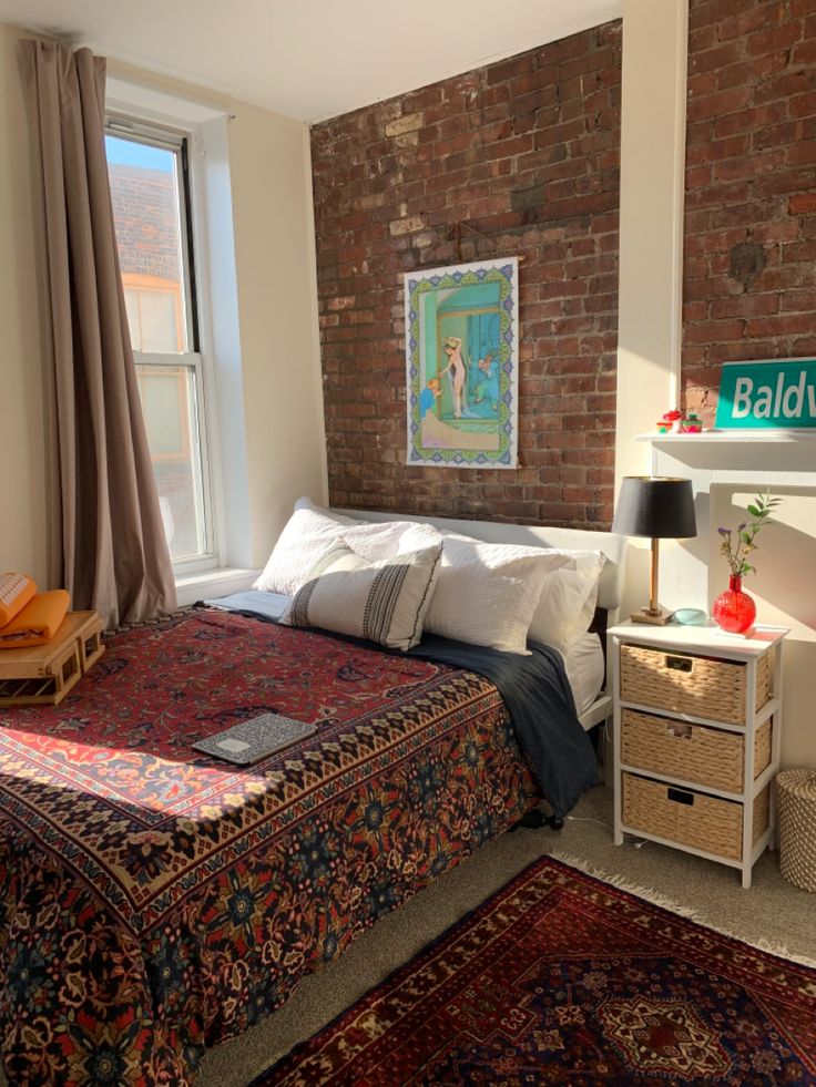 a bedroom with a brick wall, bed and rugs in front of the window