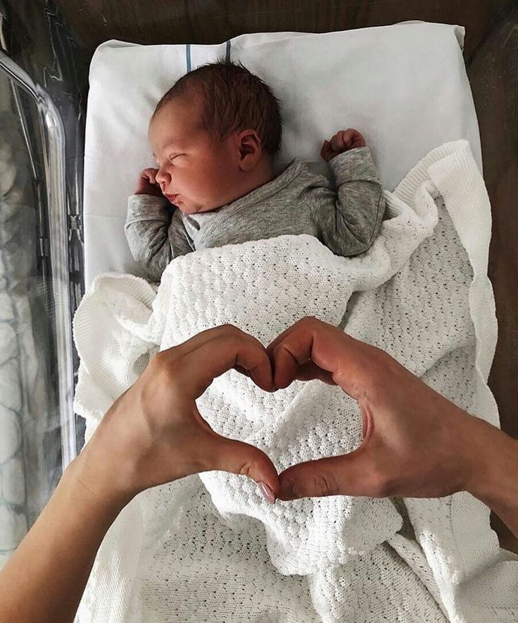 a person holding a baby in the shape of a heart while laying on top of a bed