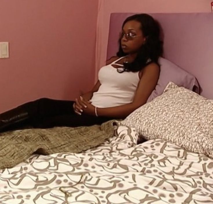 a woman sitting on top of a bed in a room with pink walls and pillows