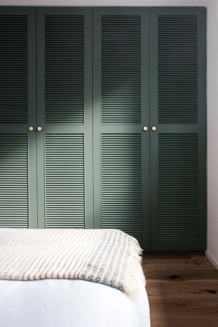 a bedroom with green shutters on the wall and a white bed in front of it