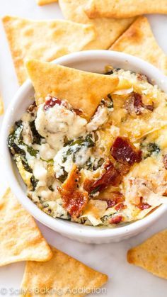 spinach dip with bacon and cheese in a white bowl surrounded by tortilla chips