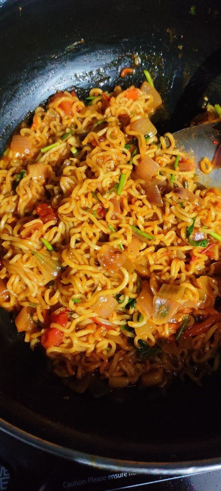 a wok filled with noodles and vegetables on top of a stove