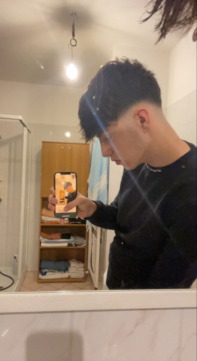 a man standing in front of a bathroom mirror looking at his cell phone while taking a selfie