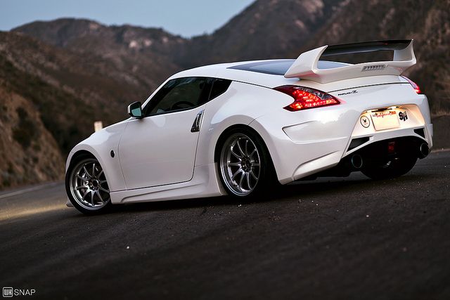 the rear end of a white sports car on a road with mountains in the background