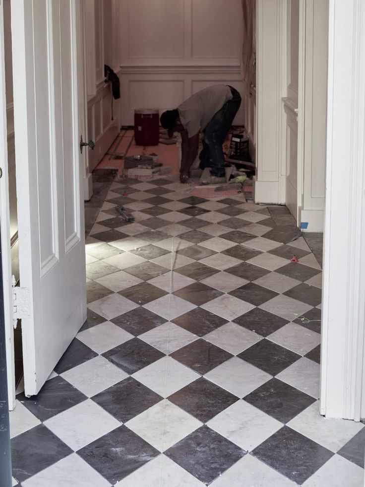 a man working on a checkered floor in an empty room with two doors open