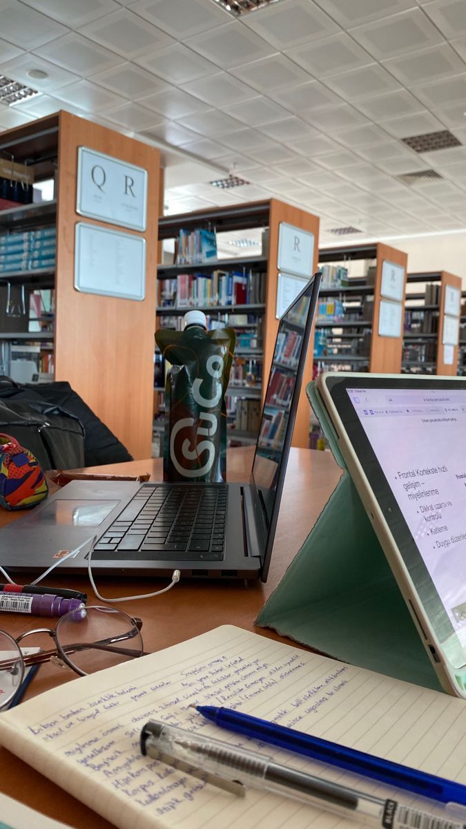 an open laptop computer sitting on top of a wooden desk next to a book shelf