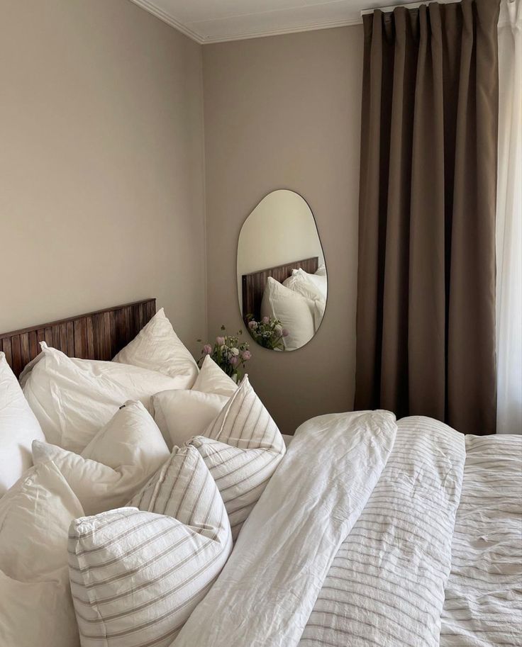 an unmade bed with white sheets and pillows in front of a round mirror on the wall