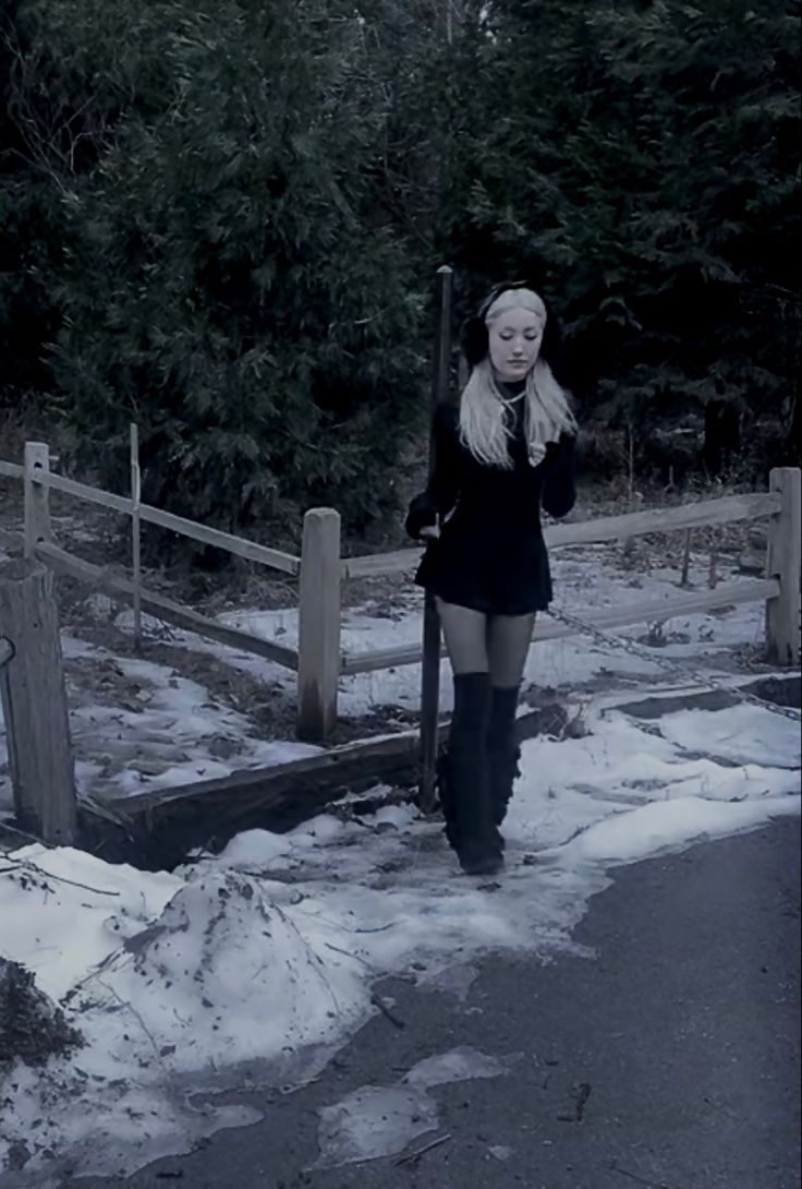 a woman is standing in the snow near a fence