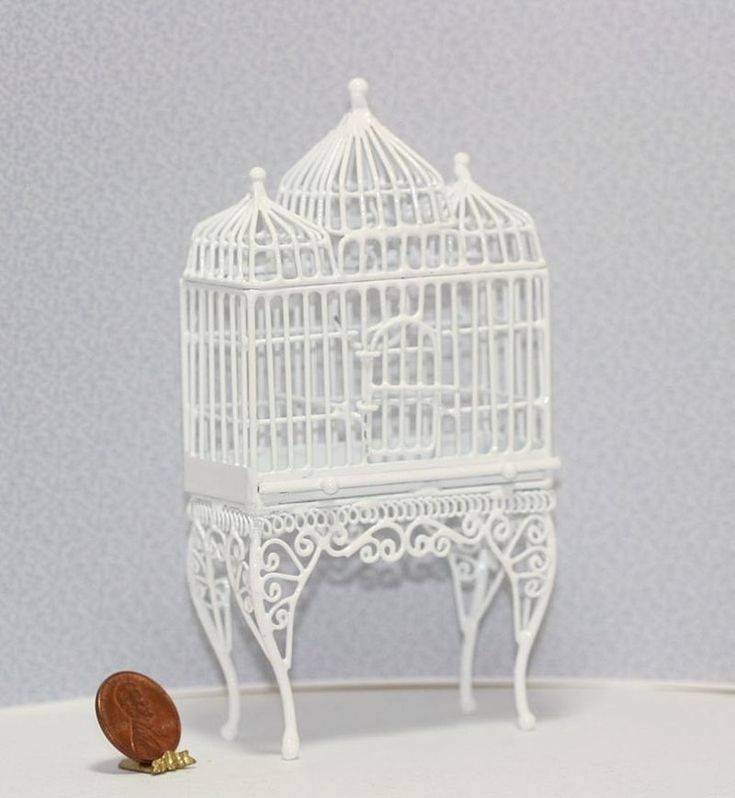 a white birdcage with a penny sitting in front of it on a table