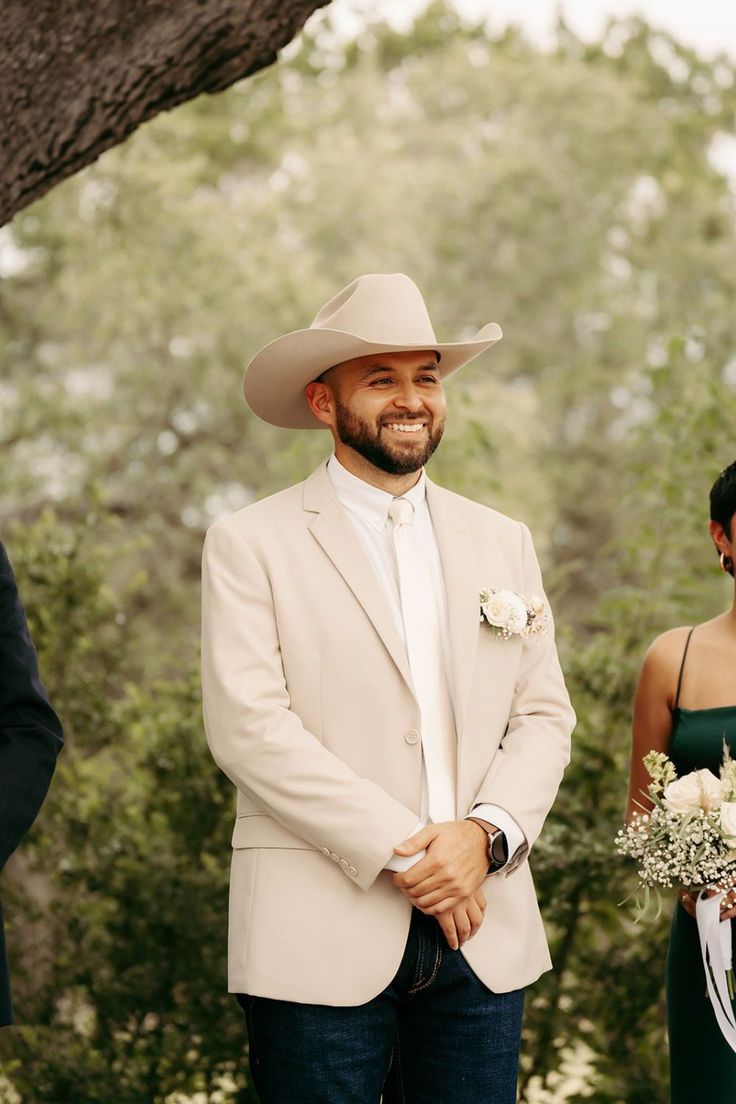 a man in a cowboy hat smiles as he stands next to his bride and groom