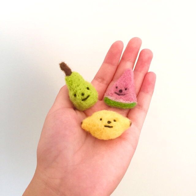 two small felt fruits are in the palm of someone's hand