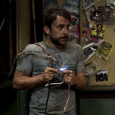 a man holding a camera in front of a wall covered with stickers and magnets