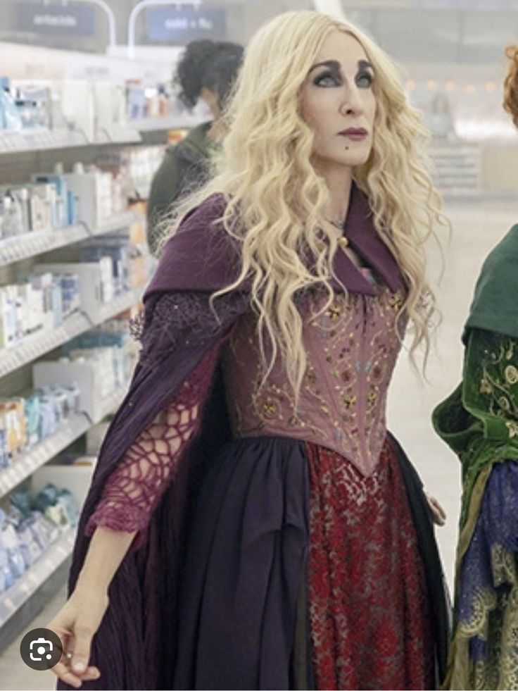 two women dressed in medieval clothing standing next to each other near shelves with products on them