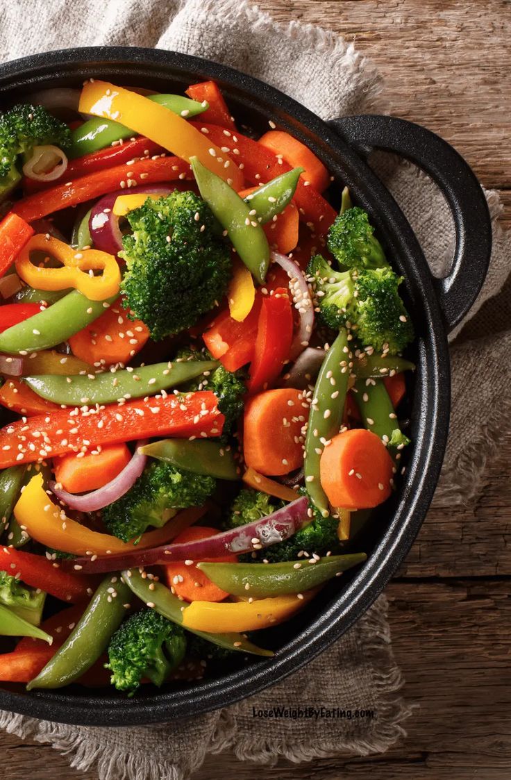 a skillet filled with vegetables on top of a wooden table next to a towel