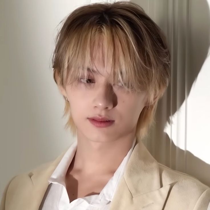 a young man with blonde hair wearing a beige suit and white shirt looking at the camera