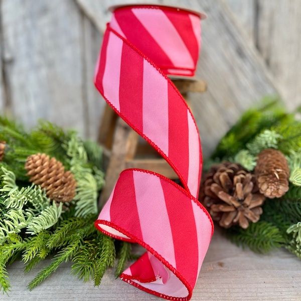 a red and white striped ribbon with pine cones on the side next to evergreen branches