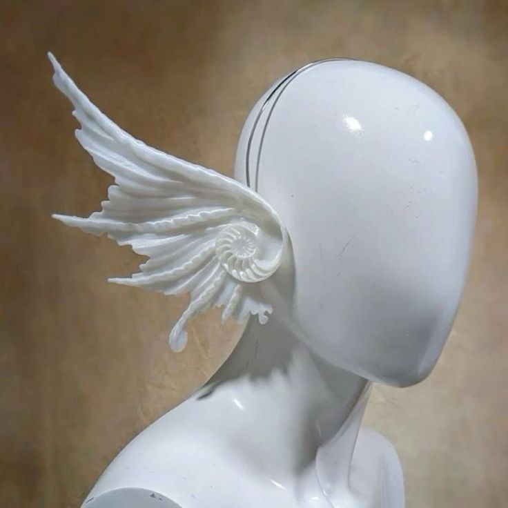 a white mannequin head with angel wings on it's back, against a brown background