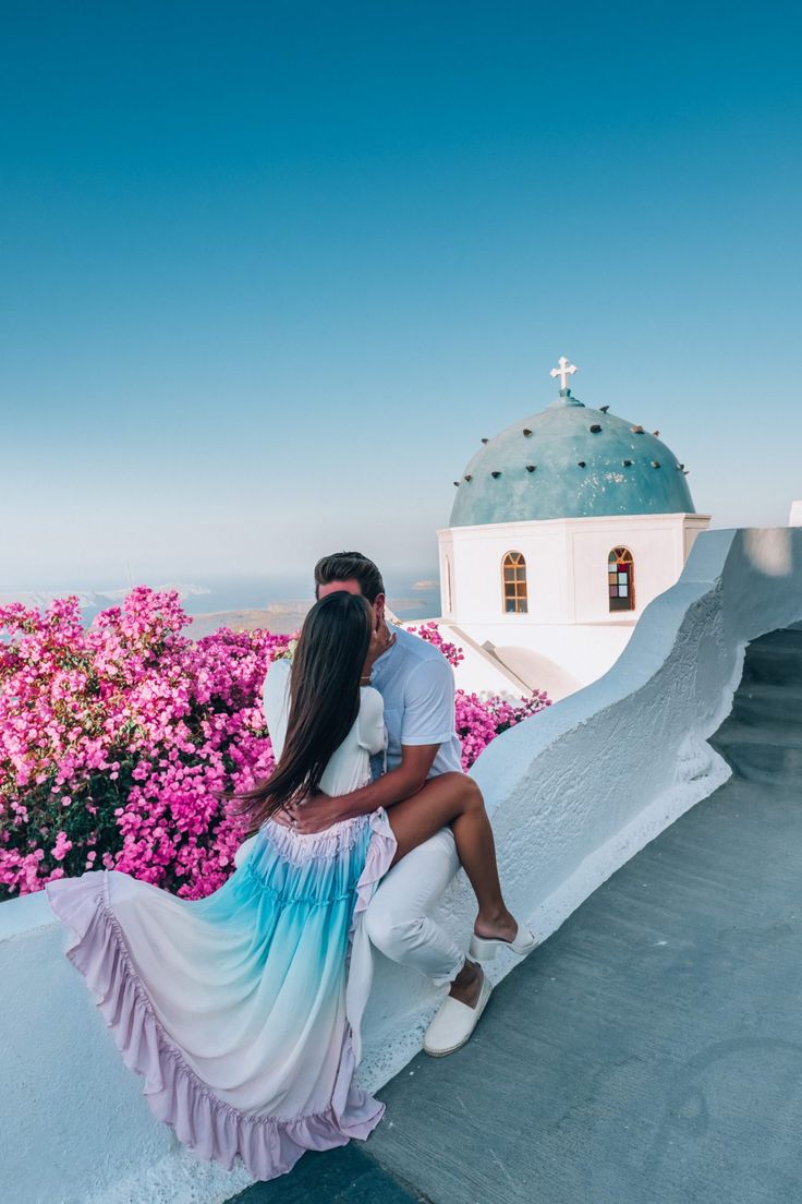 a man and woman sitting on the edge of a building with flowers in the background