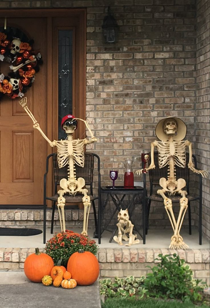 two skeletons sitting on the front porch with pumpkins